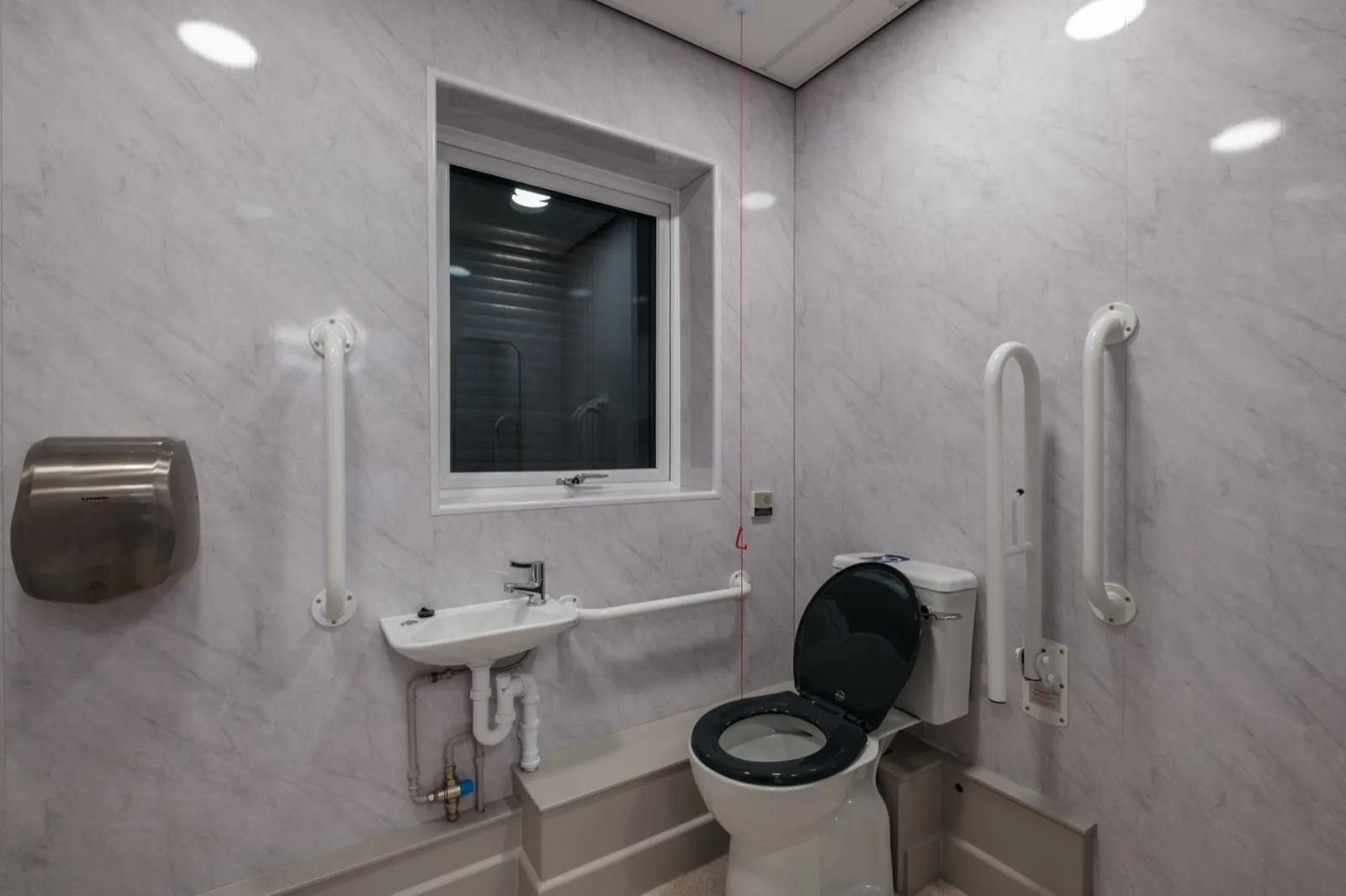 DDA-compliant accessible bathroom with marble-effect wall panels and grab rails at Boluda Towage